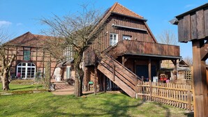 Een rustiek houten gebouw met een steil dak, een houten trap en een omheind gebied met een houten hek.