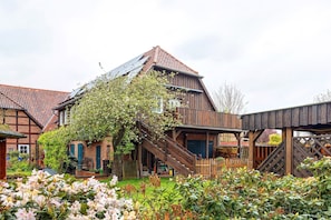 A traditional wooden house with a steeply pitched roof, a wooden staircase, and a garden with flowering plants. - Holiday Apartment Oertzheide with Private Garden, Balcony and Wi-Fi (Südheide)