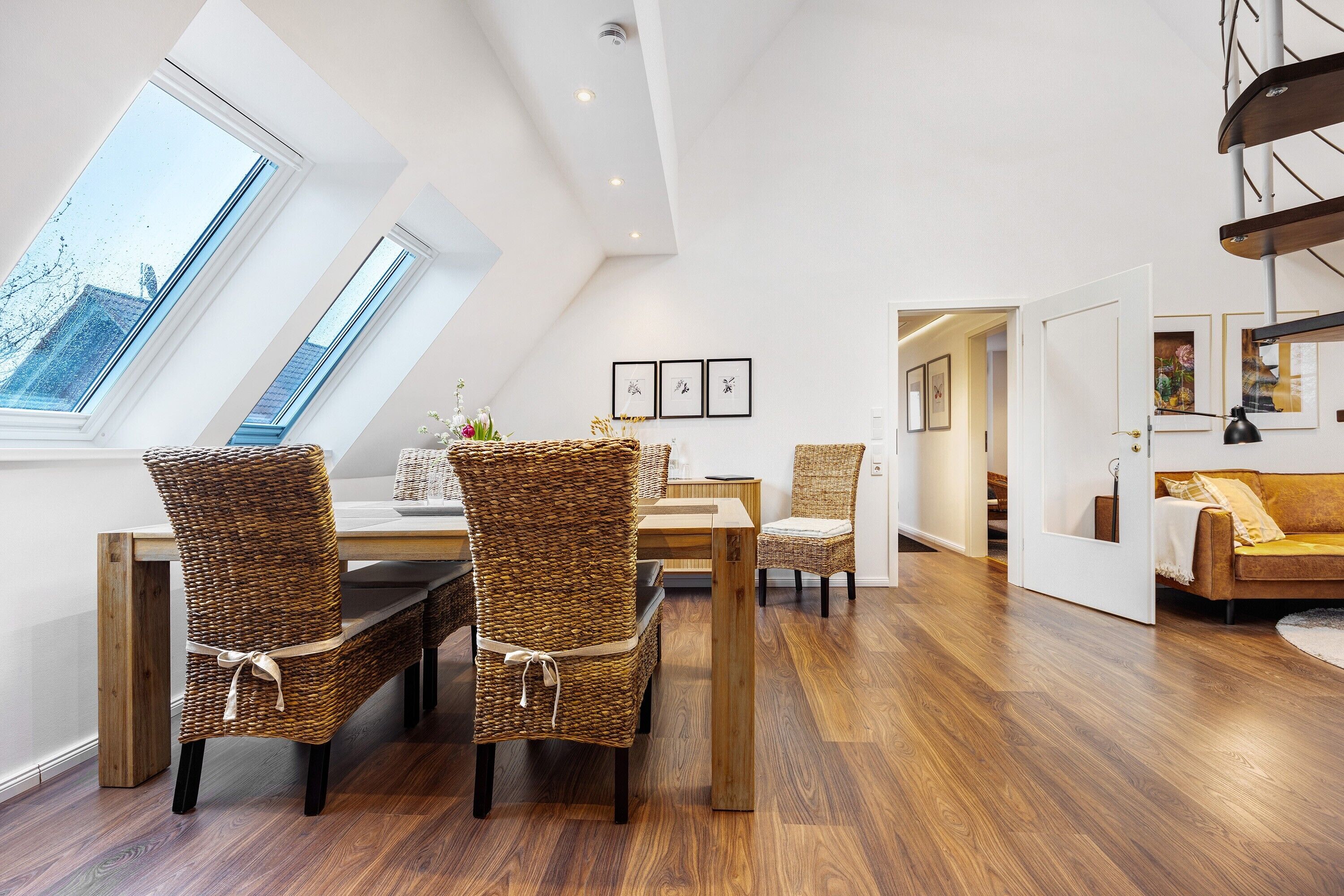 Um loft moderno com área de refeições, cadeiras de vime, mesa de madeira e vista através de claraboias.