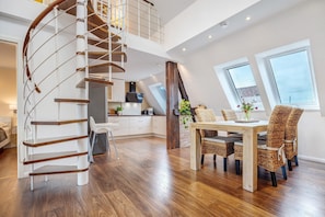 A spacious loft-style apartment with a spiral staircase, a dining area with wicker chairs, and a kitchen with white cabinets. - Holiday Apartment Oertzheide with Private Garden, Balcony and Wi-Fi (Südheide)