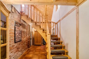 A wooden staircase with a handrail, a brick wall with a framed picture, and a tiled floor.