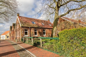 A traditional brick building with a red-tiled roof, a paved pathway, and a green hedge.
