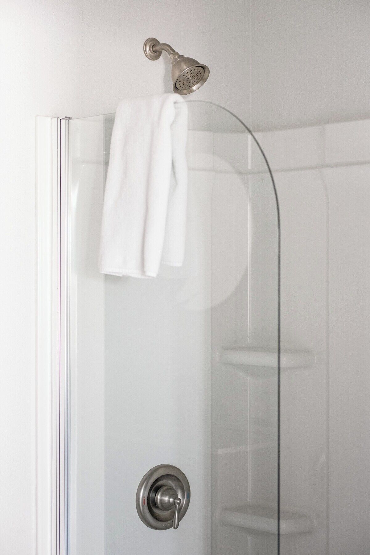 A glass shower enclosure with a metallic showerhead and a towel hanging on the door.