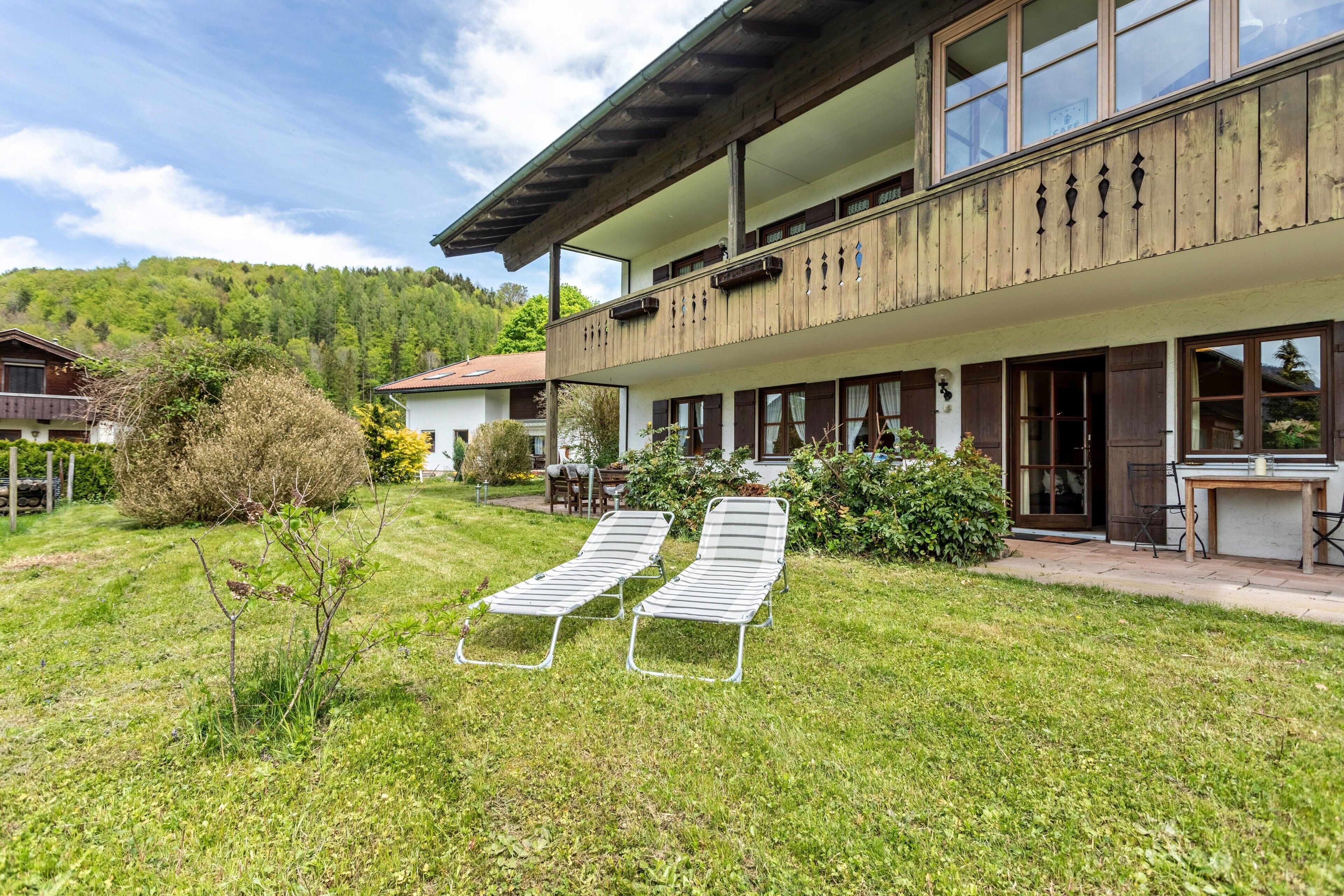Un edificio de dos pisos con balcón, un pequeño jardín con dos sillones de relax y una zona de comedor con mobiliario exterior.