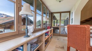 A room with large windows, a wooden bookshelf, a wicker chair, and a ceiling light fixture.