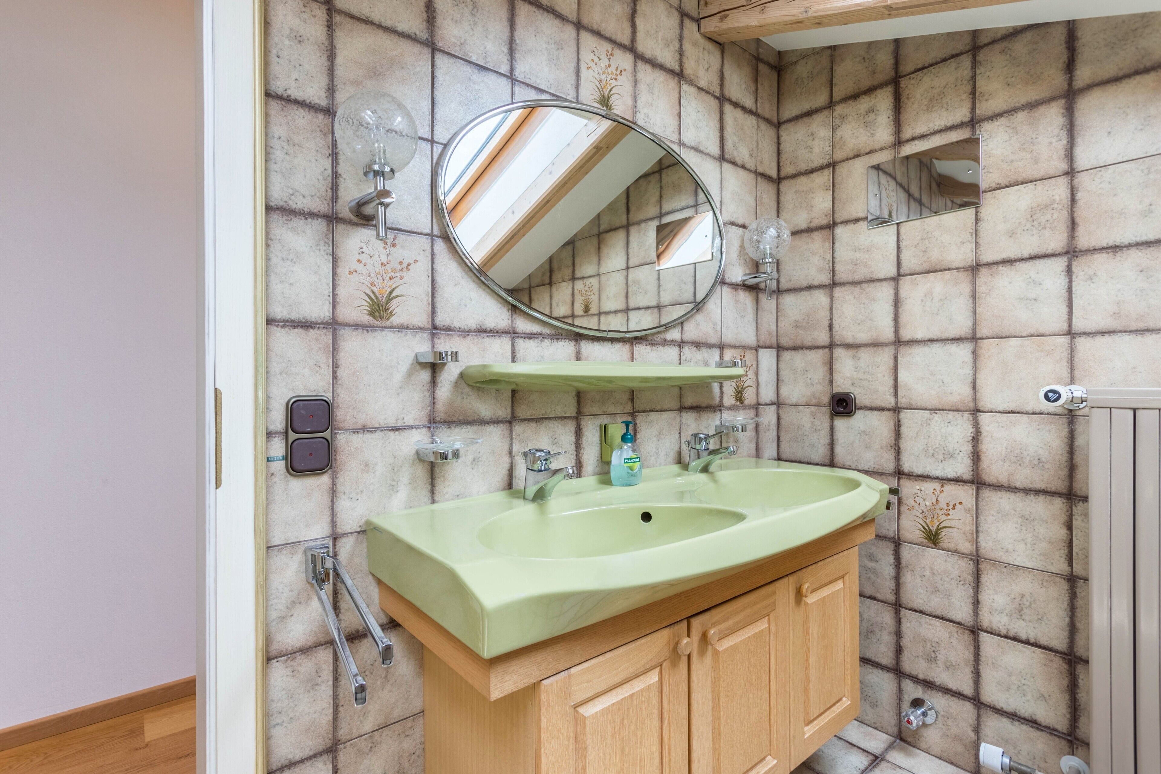 Un baño con un lavamanos verde, armarios de madera, un espejo y un revestimiento de azulejos.