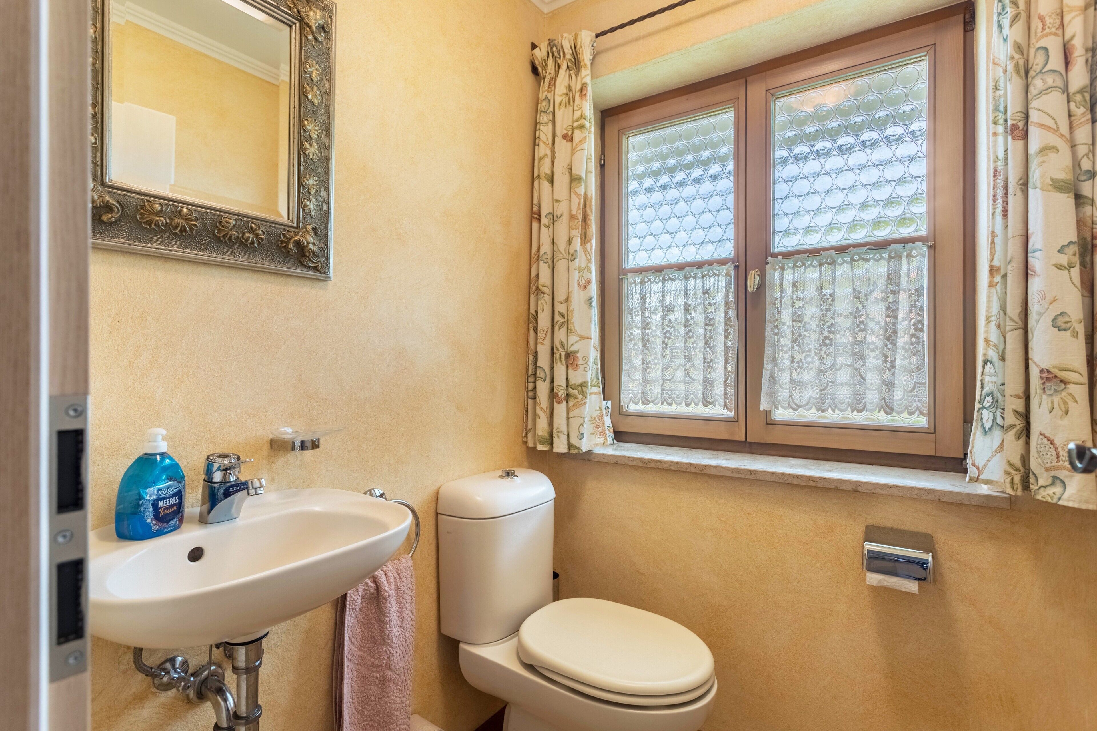 A bathroom with a sink, toilet, and window with patterned curtains.