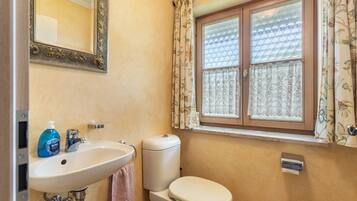 A bathroom with a sink, toilet, and window with patterned curtains.