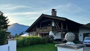 A chalet with a wooden facade, a stone chimney, and a view of mountains in the background.