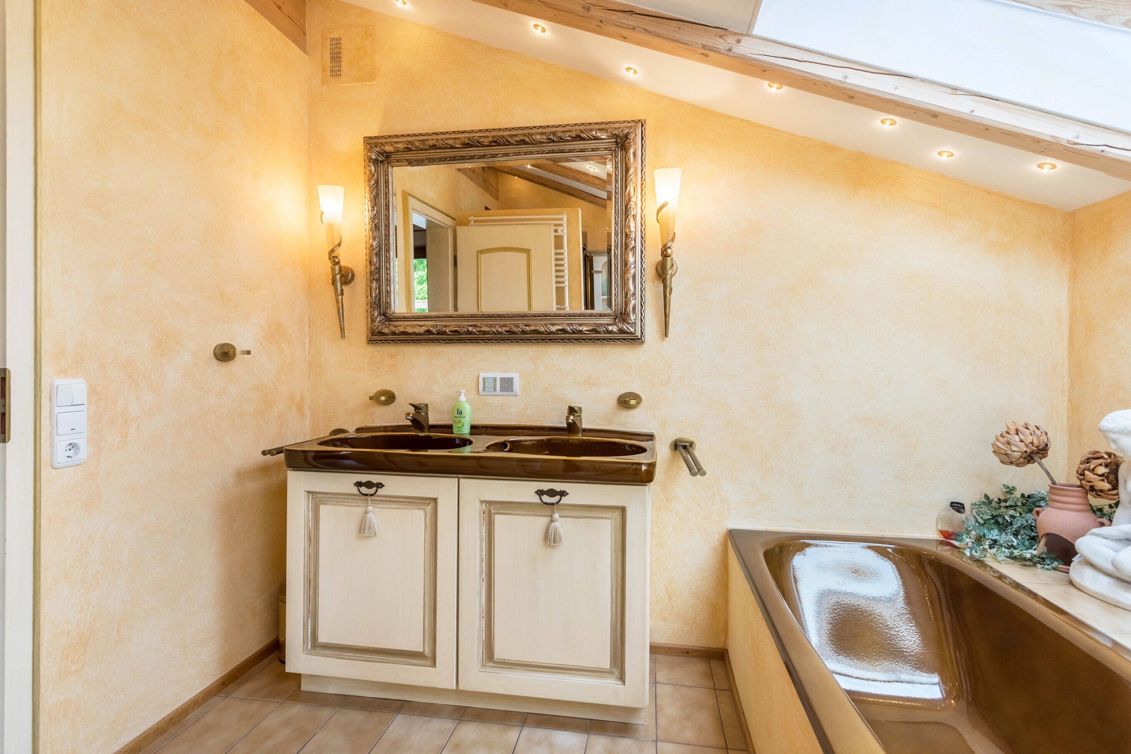 A bathroom with a double sink, a mirror, wall sconces, and a towel rack.