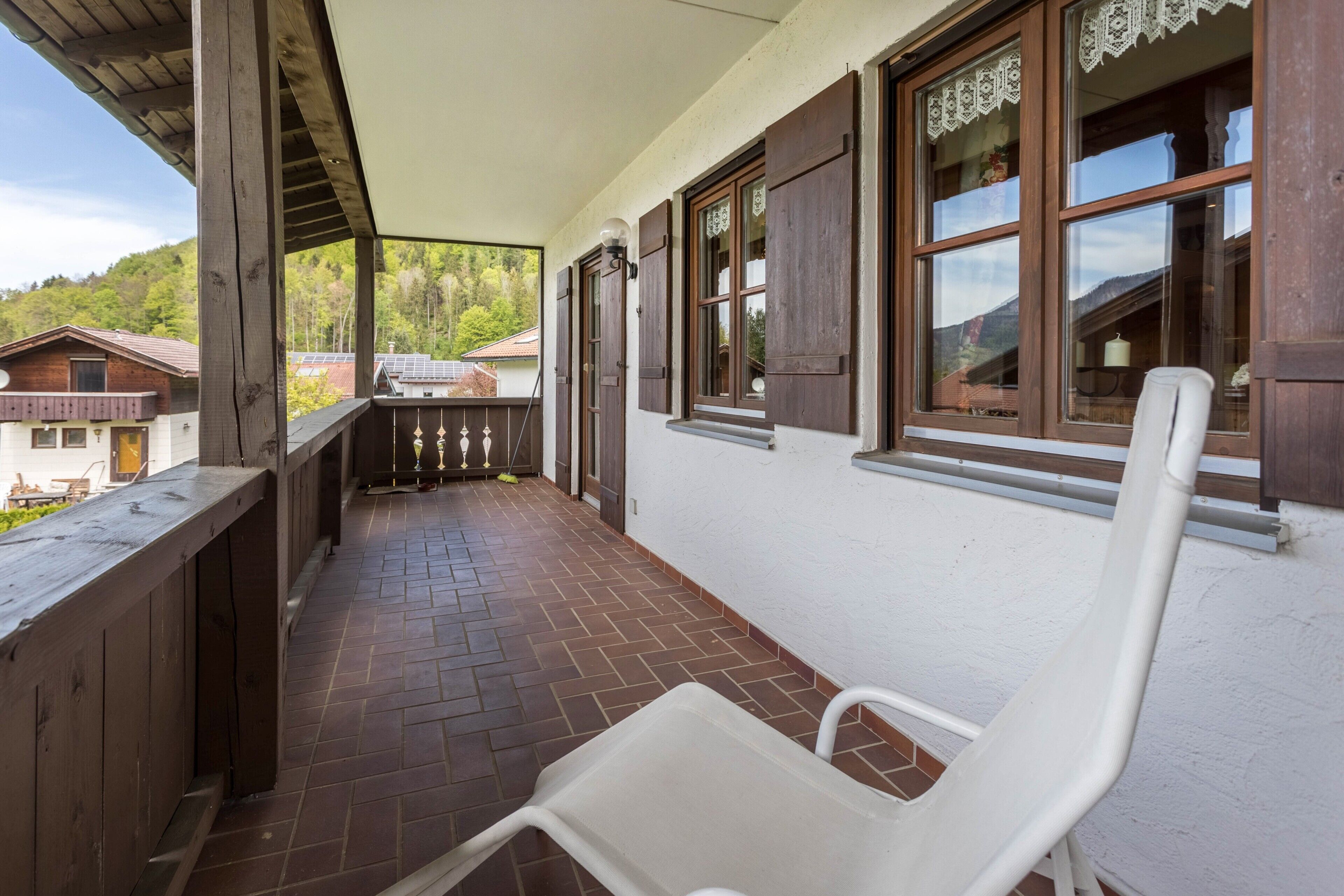 Ein überdachter Balkon mit einem weißen Kunststoffstuhl, Holzgeländern und Blick auf die umliegenden Gebäude.