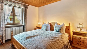 A bedroom with a wooden headboard, a bed with a quilt, two bedside tables with lamps, and a window with curtains. - Holiday Home Bergblick for 4 Guests (Unterwössen)