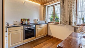 A kitchen with wooden cabinets, a stove, a sink, and a window with curtains. - Holiday Home Bergblick for 4 Guests (Unterwössen)