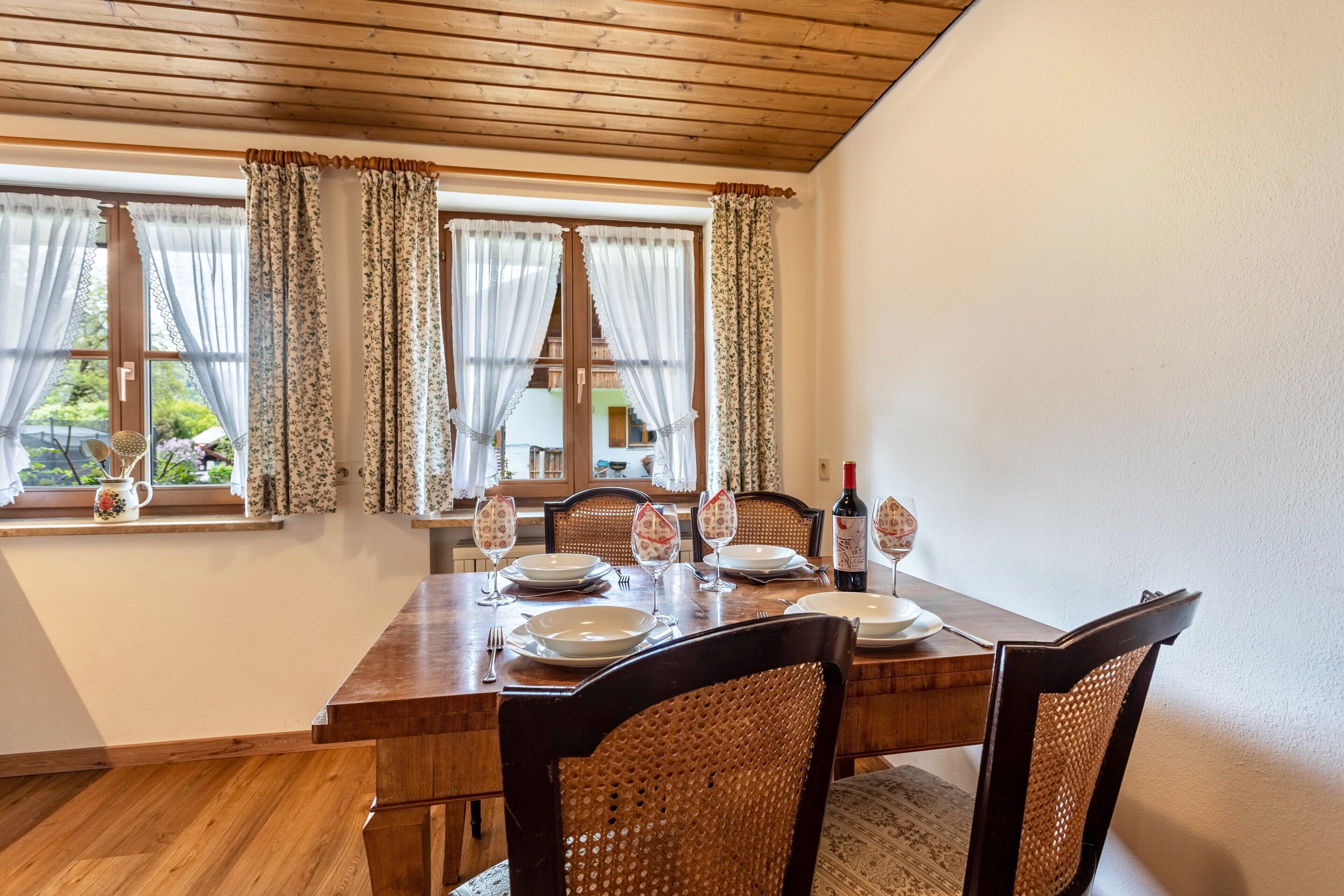 Ein Essbereich mit Holztisch, gedeckt für vier Personen, umgeben von Korbstühlen und Blick auf Grünflächen.