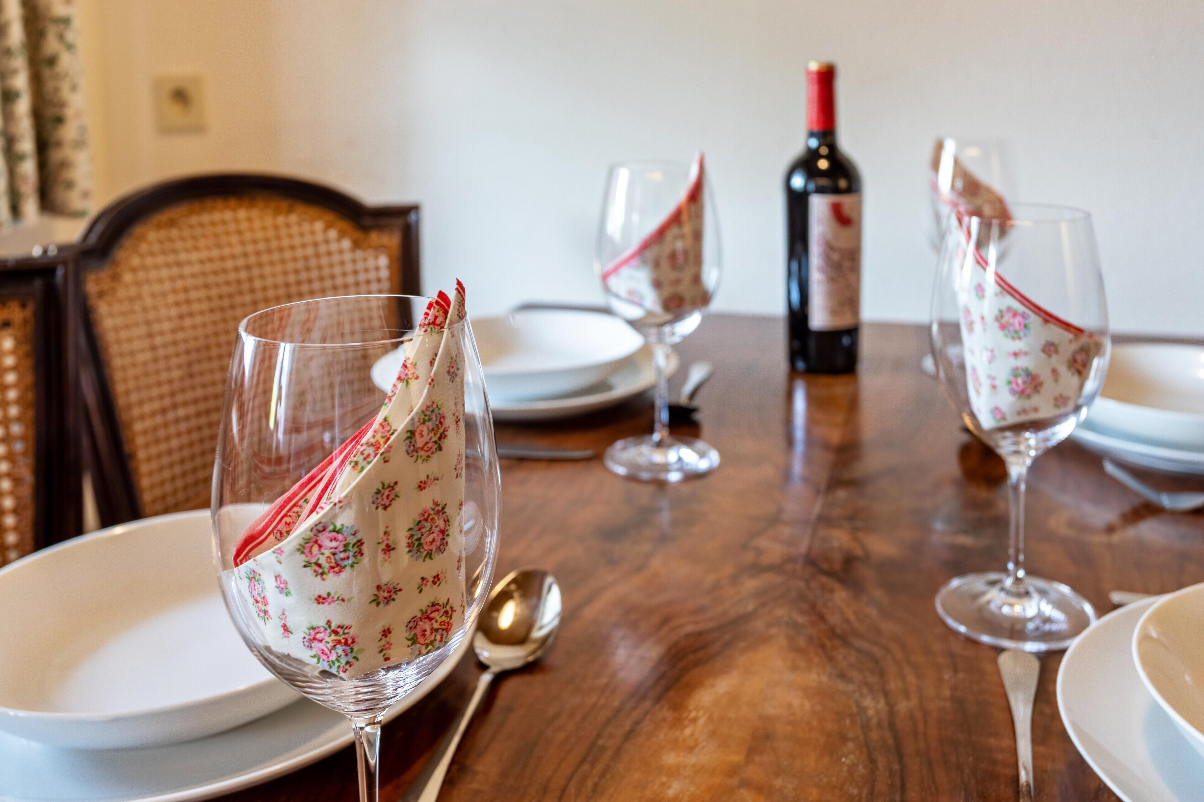 Een eettafel met servetten met bloemenprint, wijnglazen en een fles wijn.