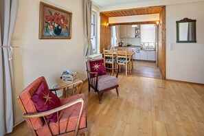 Et værelse med trægulv, et spisebord med stole, en radiator, et lille bord med en kasse og et billede på væggen.