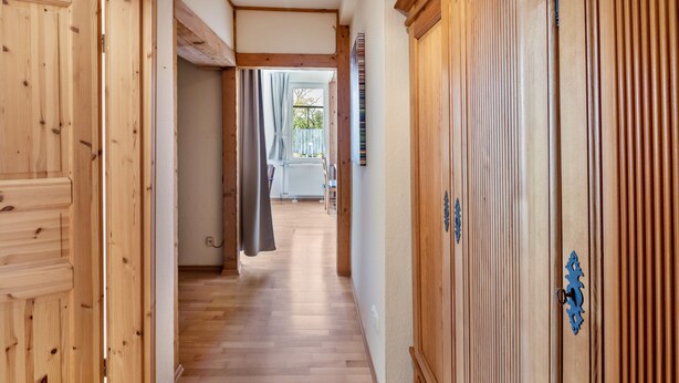 Un pasillo con pisos de madera y puertas, que conduce a una habitación con ventana y cortinas.