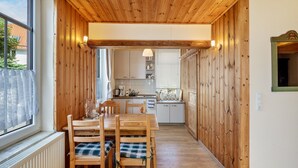 Un interior de madera con una mesa y sillas de comedor, una zona de cocina con armarios y un ventanal.