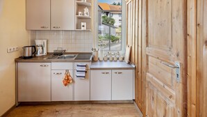 Una cocina con armarios blancos, un lavamanos de acero inoxidable y una ventana con vistas a una zona residencial.