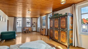 A room with wooden ceiling, a bed, a green sofa, a wooden cabinet, and a window with curtains.