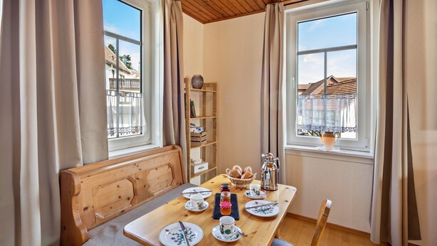 A dining area with a wooden table, chairs, a bench, and a bookshelf.