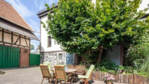 A courtyard with a table and chairs, a green fence, and a tree.