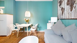 A modern living room with teal walls, a white sofa, and a dining area with white chairs and a table.