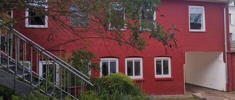 Een rood gebouw met witte ramen, een zichtbare trap en een kleine tuin.