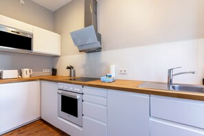 A compact kitchen with white cabinetry, a stainless steel sink, a built-in oven, and a microwave.