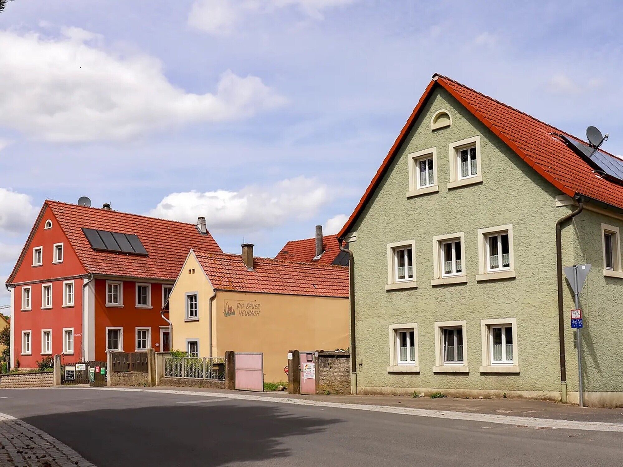 Rivissä värikkäitä taloja, joiden katoilla on aurinkopaneelit, katu ja kirkas taivas.