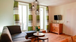 Un salon comprenant un canapé, une petite table ronde, un meuble et un téléviseur.