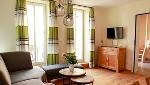 A living room with a sofa, a small round table, a cabinet, and a TV. - Apartment 'Ferienwohnung Kammer' with Private Terrace, Shared Garden and Wi-Fi (Iphofen)