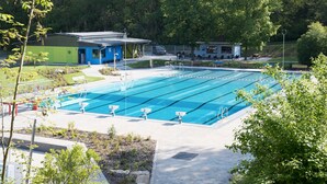 A swimming pool with lanes, a changing room, and a small building with a blue roof. - Apartment 'Ferienwohnung Stübla' with Private Terrace, Shared Garden and Wi-Fi (Iphofen)