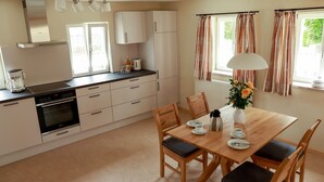 A modern kitchen with white cabinets, a built-in oven, and a coffee maker. There is a dining table with chairs and a vase of flowers. - Apartment 'Ferienwohnung Stübla' with Private Terrace, Shared Garden and Wi-Fi (Iphofen)
