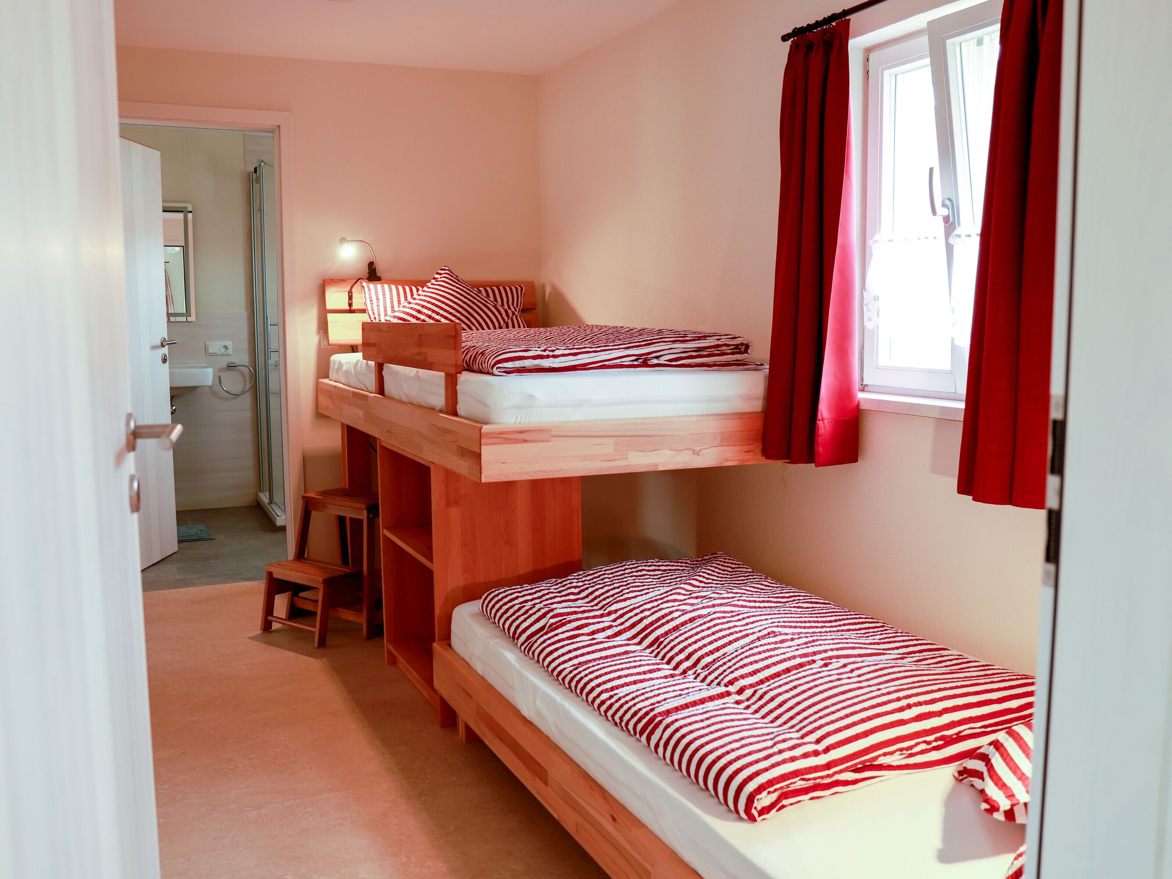 A bunk bed room with a desk and a window with red curtains.
