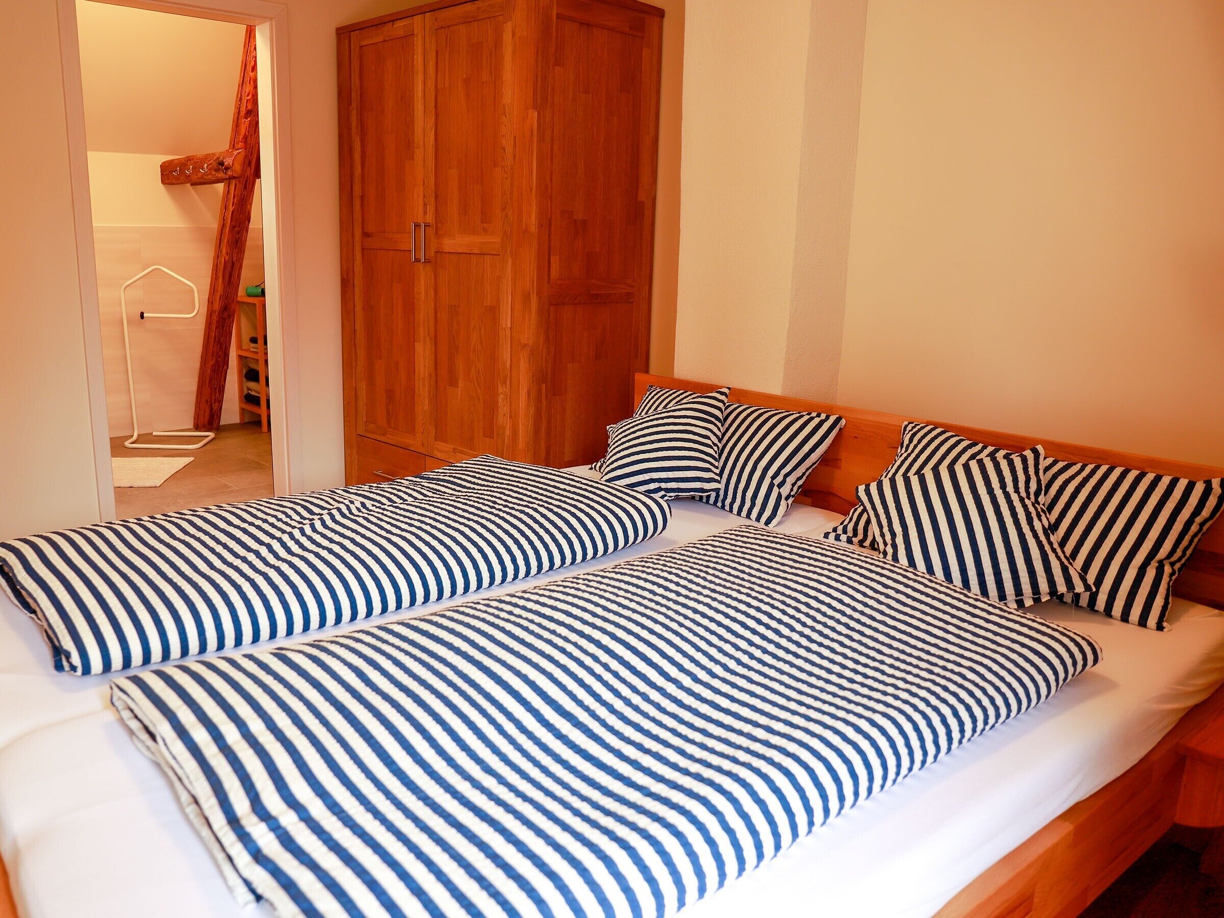 A double bed with striped bedding, a wooden wardrobe, and a door leading to a bathroom.