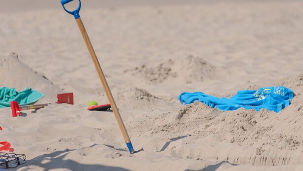 Eine Strandansicht mit einer Schaufel, einem blauen Handtuch und Strandspielzeug.