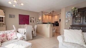 Ein gemütliches Wohnzimmer mit Essbereich, einer Küche und einer kleinen Kochinsel. Es gibt floral gemusterte Sofas und einen weißen Sessel.