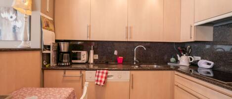 A compact kitchen with light wooden cabinets, a microwave, a coffee maker, and a sink.