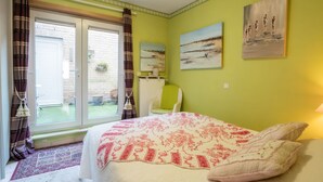 Ein Schlafzimmer mit Bett, einem Sessel, einem Gemälde und Blick ins Freie.
