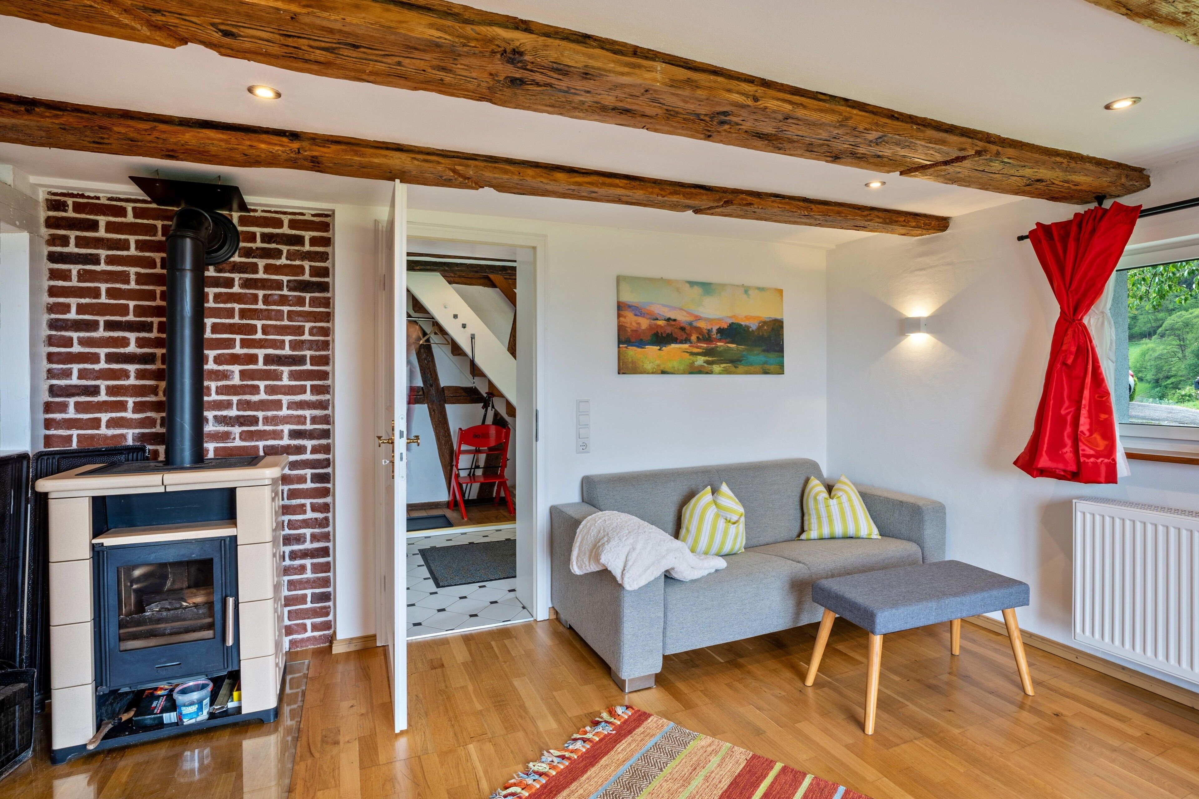 A living room with a brick fireplace, a grey sofa, and a red curtain.