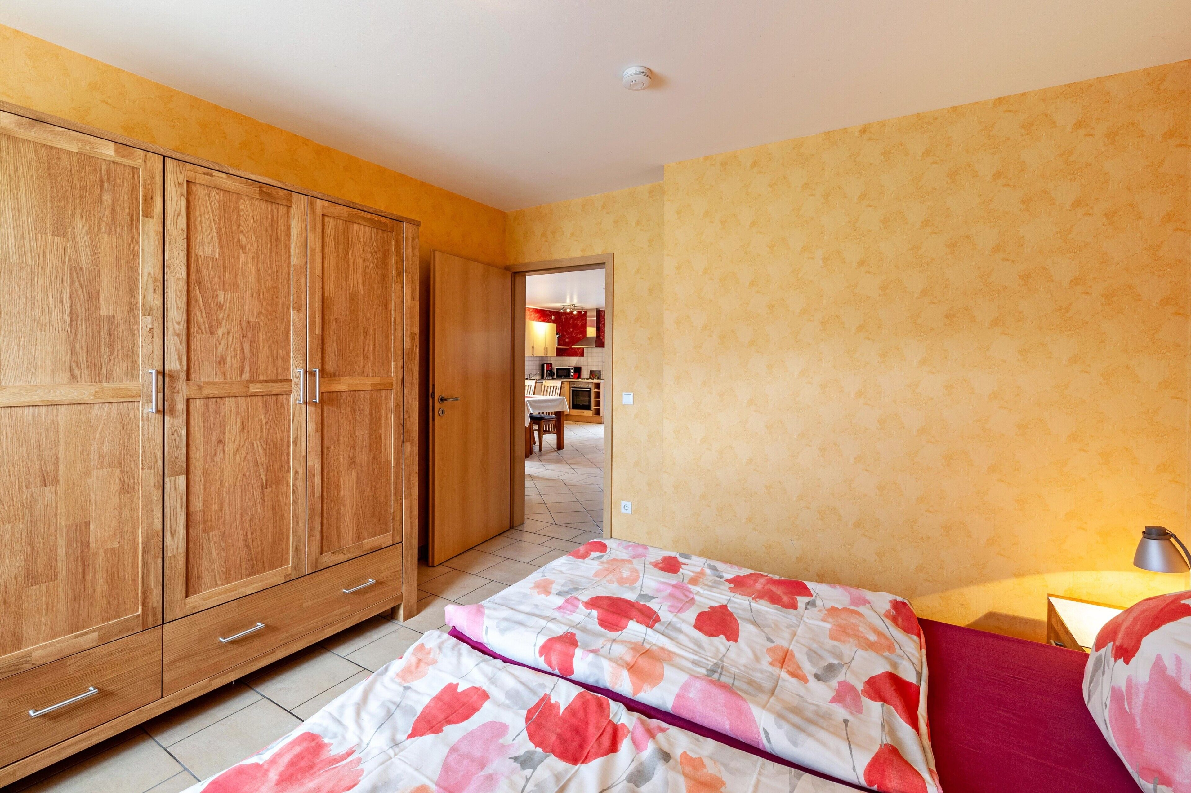 A bedroom with a bed, wooden wardrobe, and a view into the kitchen.