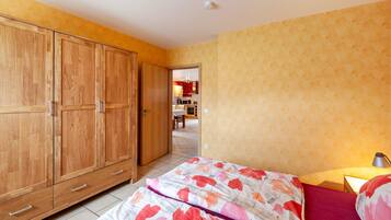 A bedroom with a bed, wooden wardrobe, and a view into the kitchen.