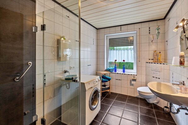 Une salle de bain moderne avec une douche à parois de verre, un lave-linge, des toilettes et un lavabo avec un miroir.