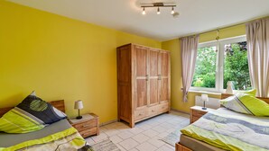 Ein Schlafzimmer mit zwei Betten, einem Kleiderschrank, einem Fenster mit Vorhängen und einem Nachttisch mit Lampe.