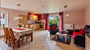 Eine moderne Küche mit Essbereich, ein Wohnzimmer mit Sofa und Couchtisch sowie ein Blick ins Freie.
