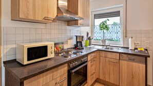 A modern kitchen with wooden cabinets, a microwave, stove, and a window with a view of buildings. - Apartment 'Tulpe' with Balcony and Wi-Fi (Kalkar-Wissel)