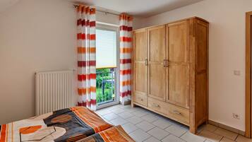 Ein Schlafzimmer mit Bett, Schrank, Heizkörper und einem Fenster mit Vorhängen.