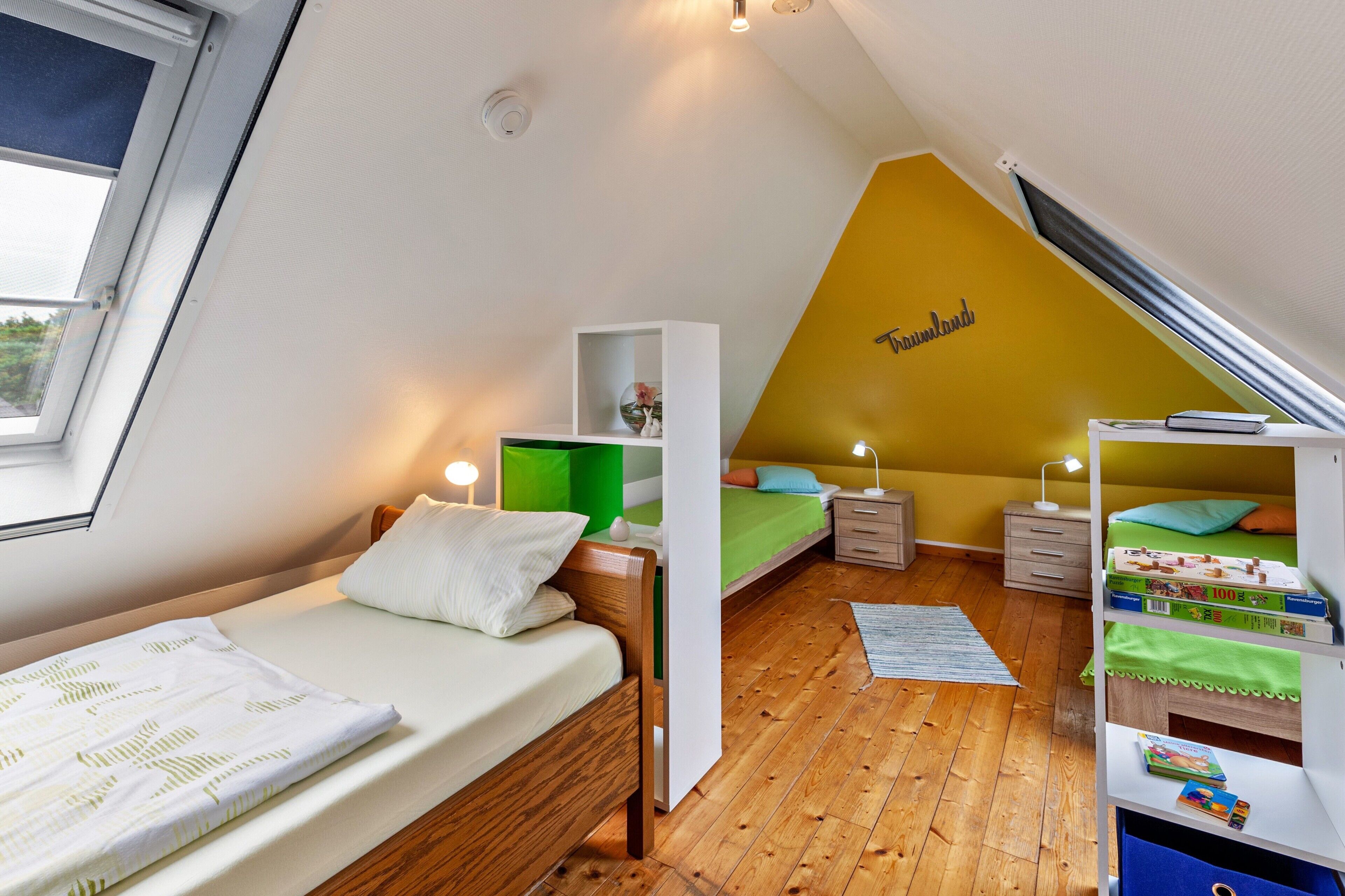 A bedroom with a sloped ceiling, a bed, a desk, a bookshelf, and a window.