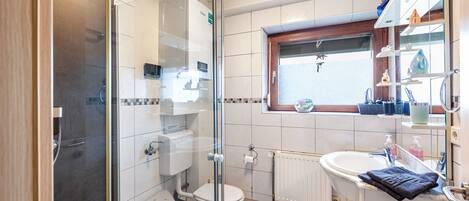 Een badkamer met een douchecabine, toilet, wastafel en raam.